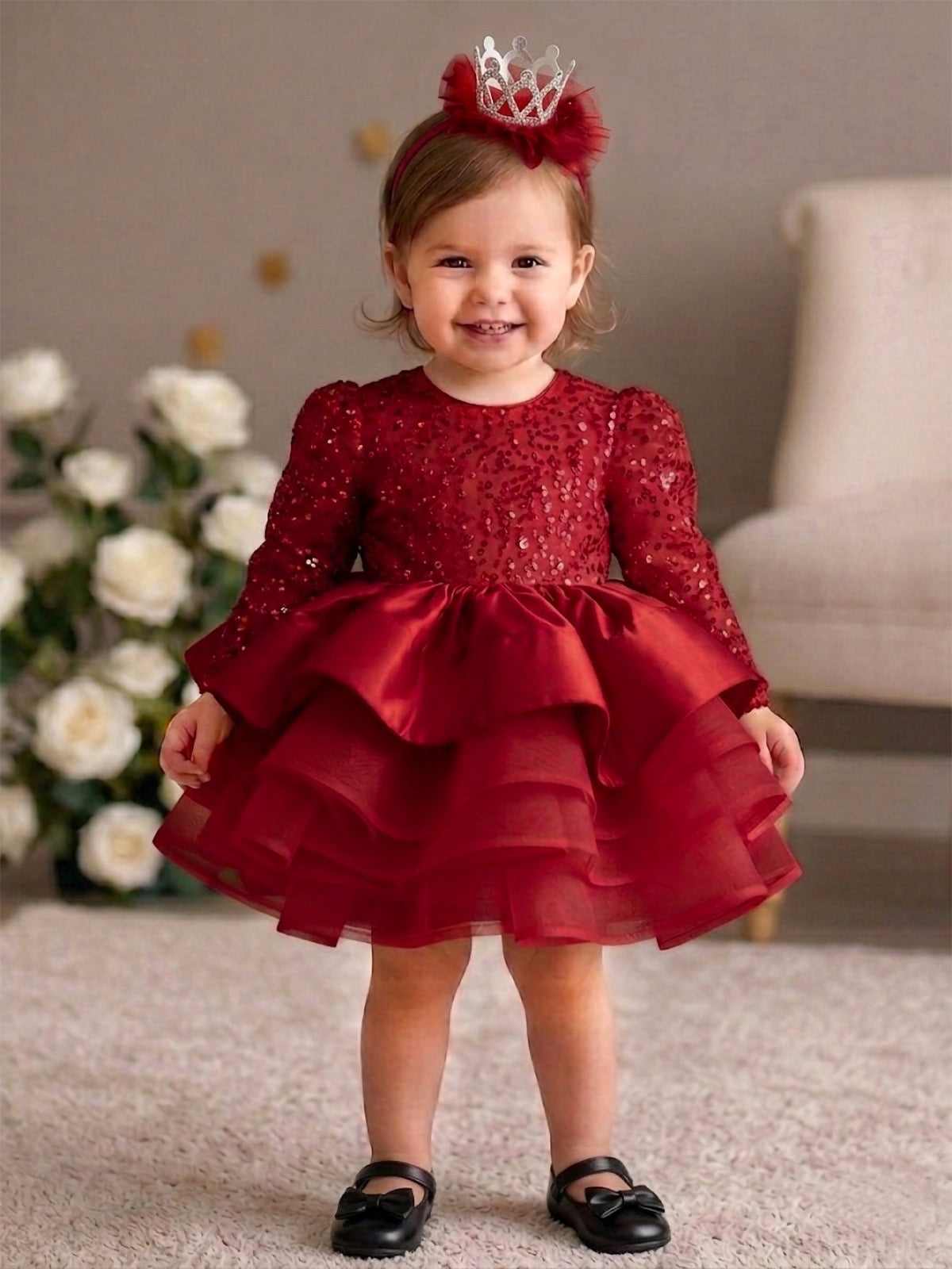 A young girl wearing a burgundy party dress with a silver crown